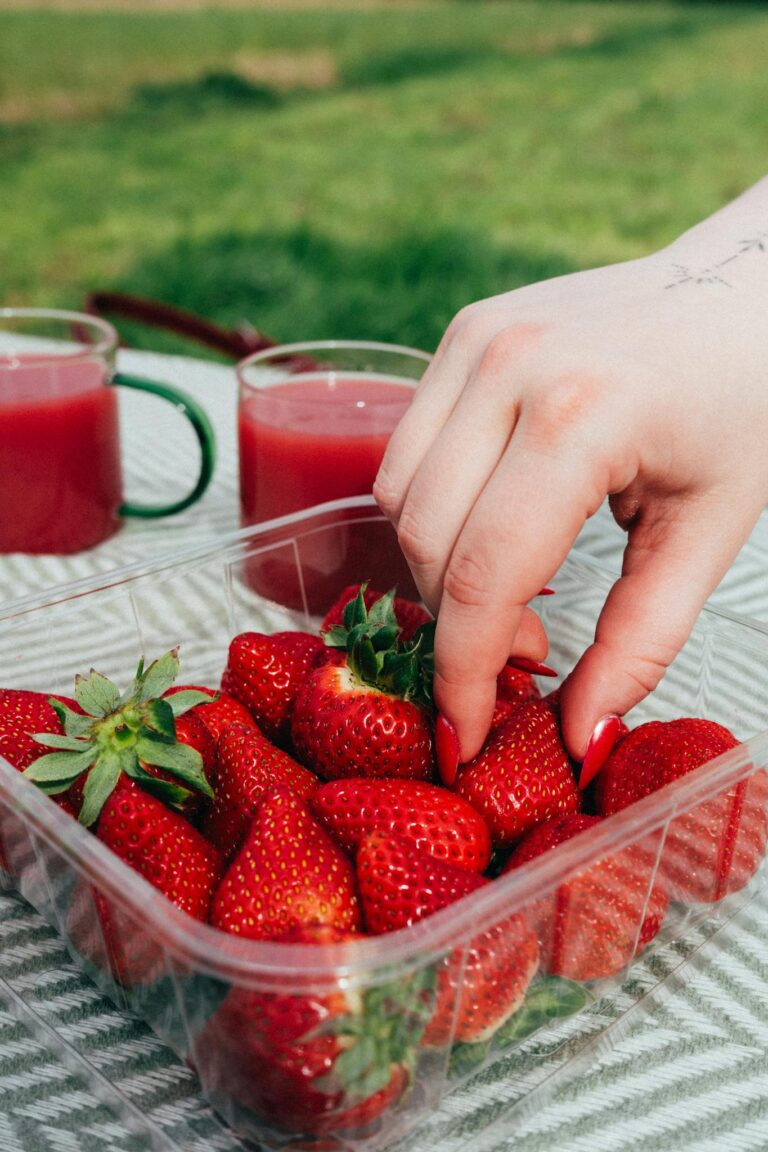 A hand reaching for fresh strawberries at an outdoor picnic, symbolizing healthy eating.